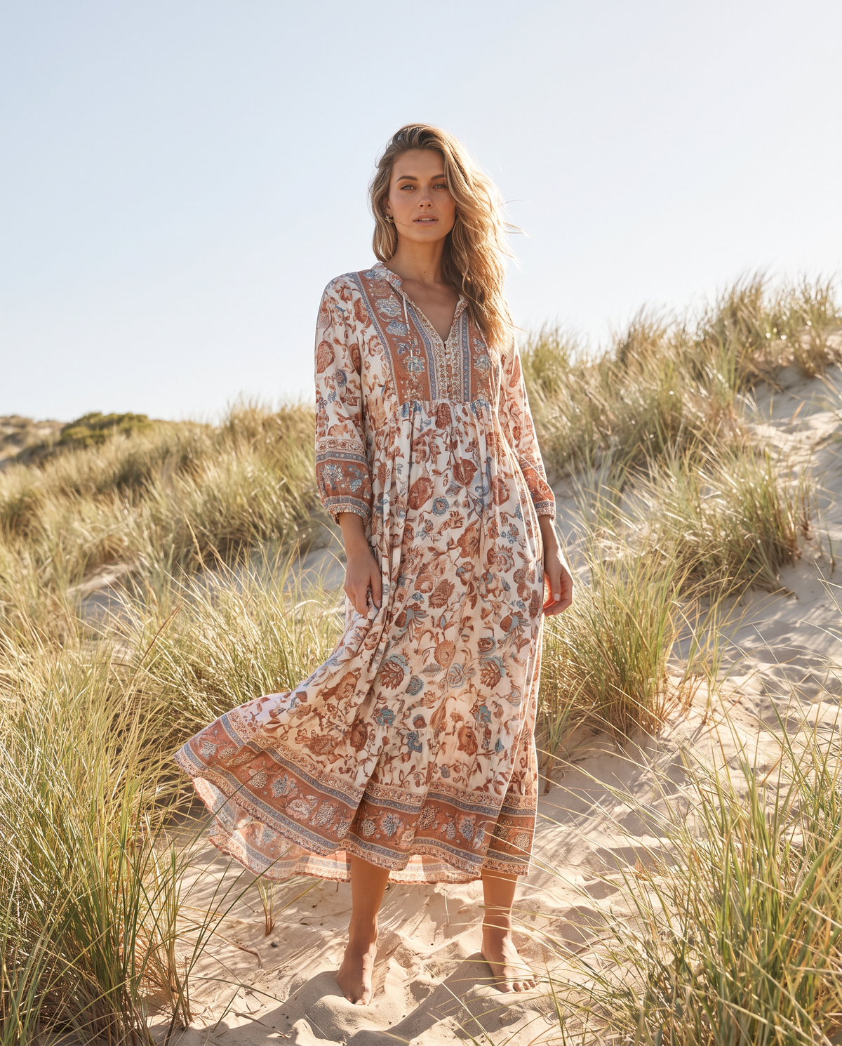 Woman in a floral print maxi dress standing in coastal sand dunes with beach grasses